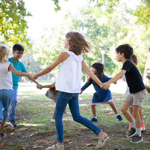 Group of children holding hands and dancing around, enjoying outdoor activities and having fun in park. Kids party or friendship concept