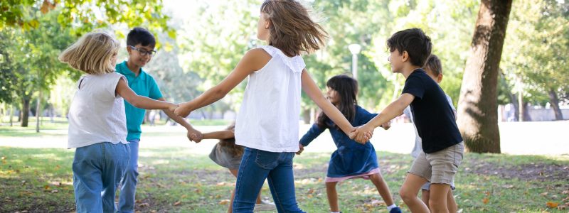 Group of children holding hands and dancing around, enjoying outdoor activities and having fun in park. Kids party or friendship concept